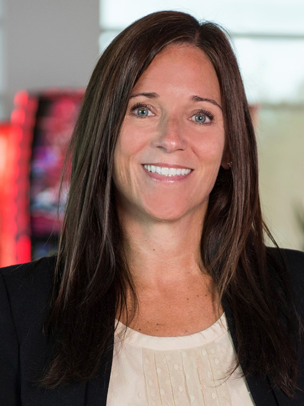 Photo of Rachel similing in front of a video slot machine wearing a black blazer and cream colored top. 