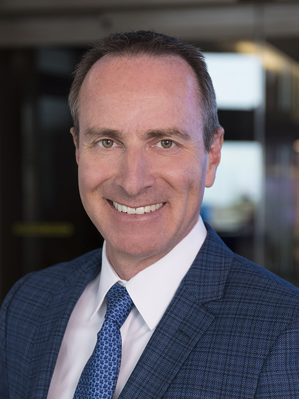 Photo of Anthony- smiling wearing a white collared shirt, blue tie, and blue suit jacket.
