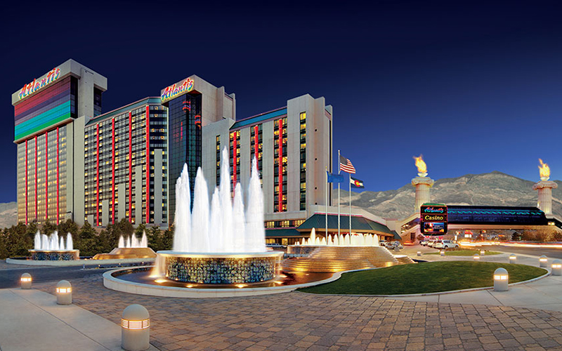 A photo of the outside of a tall casino building with red and gold lights at dusk